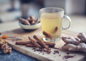 Warm winter cocktail drink in clear mug surrounded by ginger root and cinnamon sticks