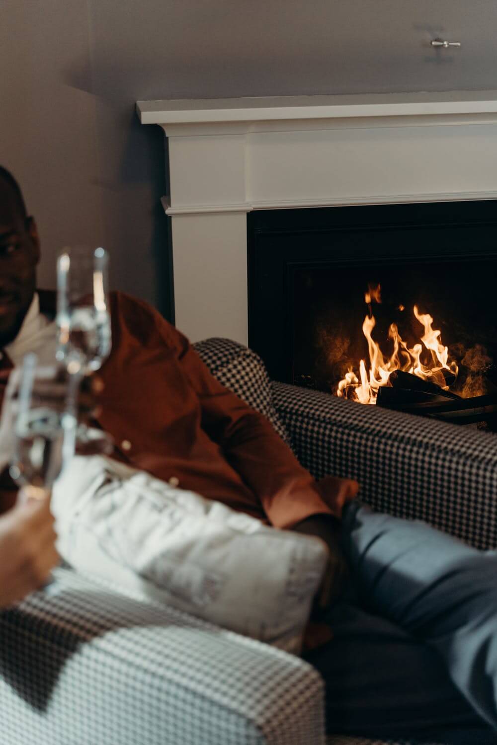 One person visible holding a champagne flute against another in front of bright fireplace
